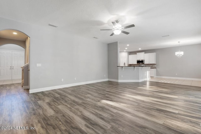 unfurnished living room featuring ceiling fan with notable chandelier and wood-type flooring