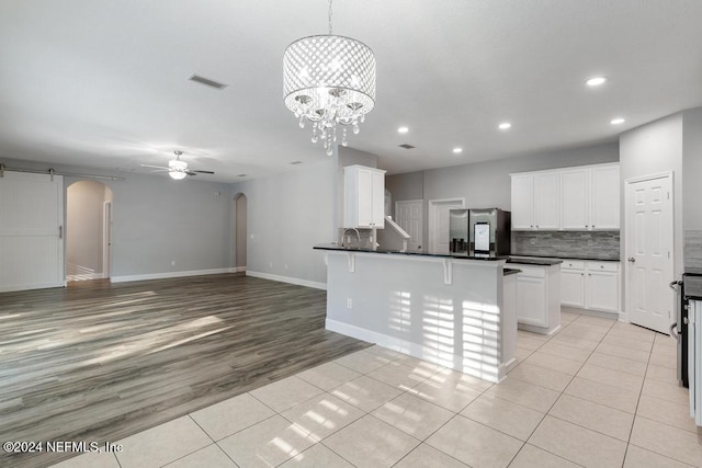 kitchen with white cabinets, ceiling fan with notable chandelier, light hardwood / wood-style floors, stainless steel fridge with ice dispenser, and a breakfast bar area