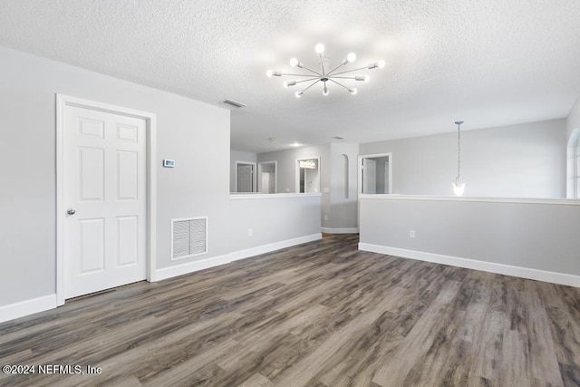 spare room featuring a textured ceiling, dark wood-type flooring, and an inviting chandelier