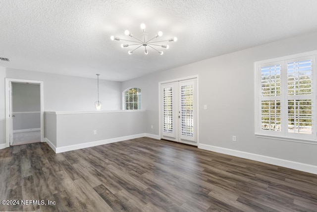 unfurnished room featuring a textured ceiling, dark hardwood / wood-style flooring, a healthy amount of sunlight, and a notable chandelier