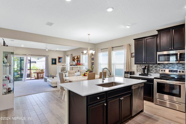 kitchen with a center island with sink, appliances with stainless steel finishes, a chandelier, light hardwood / wood-style floors, and sink