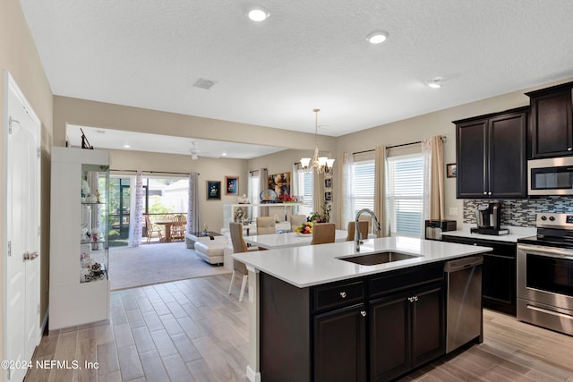 kitchen featuring appliances with stainless steel finishes, sink, a textured ceiling, light hardwood / wood-style floors, and a kitchen island with sink