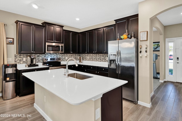 kitchen featuring light hardwood / wood-style flooring, stainless steel appliances, a center island with sink, sink, and dark brown cabinetry