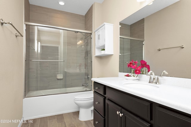 full bathroom with toilet, hardwood / wood-style floors, bath / shower combo with glass door, and vanity