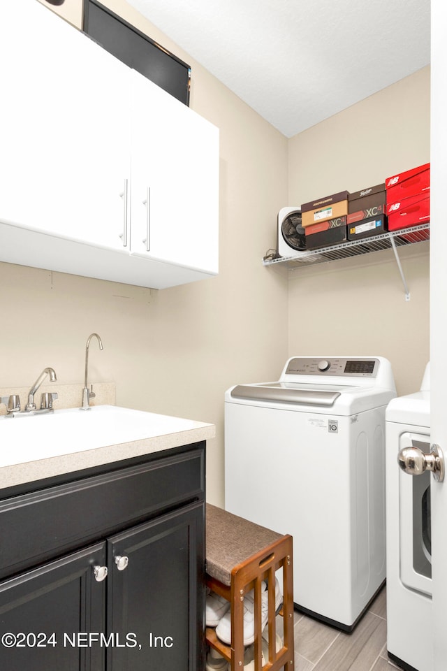 clothes washing area with sink, washer and dryer, light wood-type flooring, and cabinets