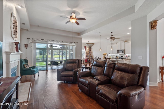 living room with ceiling fan, a textured ceiling, a tray ceiling, and dark hardwood / wood-style flooring