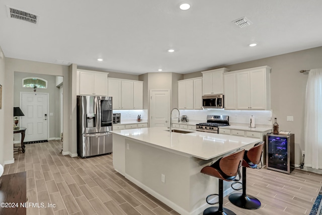 kitchen with sink, wine cooler, appliances with stainless steel finishes, white cabinets, and light wood-type flooring