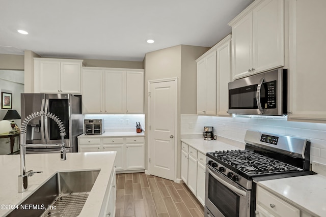 kitchen with appliances with stainless steel finishes, light hardwood / wood-style flooring, white cabinetry, and sink