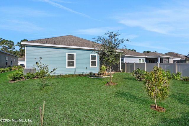 rear view of property featuring central air condition unit and a lawn