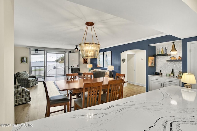 dining room featuring arched walkways, light wood-type flooring, and crown molding