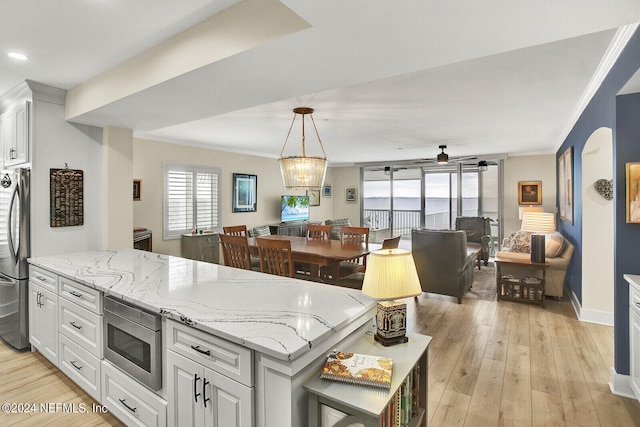 kitchen with light hardwood / wood-style flooring, white cabinetry, stainless steel appliances, light stone counters, and decorative light fixtures