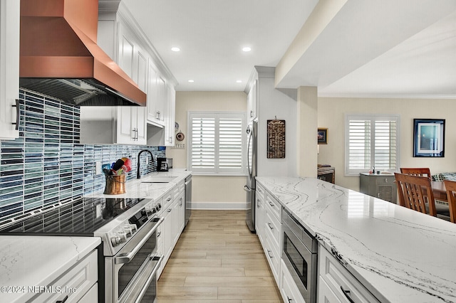 kitchen with a sink, light wood-style flooring, stainless steel appliances, wall chimney exhaust hood, and baseboards