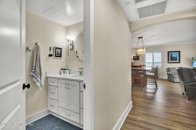 bathroom with wood finished floors, visible vents, vanity, baseboards, and a notable chandelier
