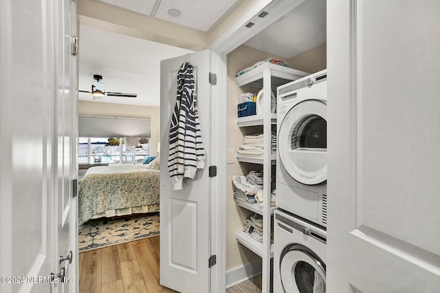 clothes washing area featuring stacked washer and dryer and wood-type flooring