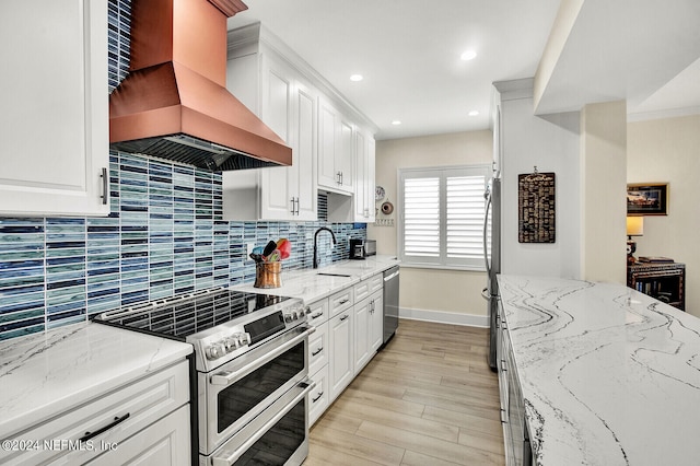 kitchen with premium range hood, white cabinets, stainless steel appliances, and a sink
