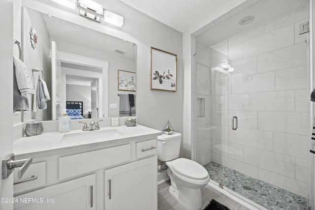 bathroom with wood-type flooring, a textured ceiling, an enclosed shower, toilet, and vanity