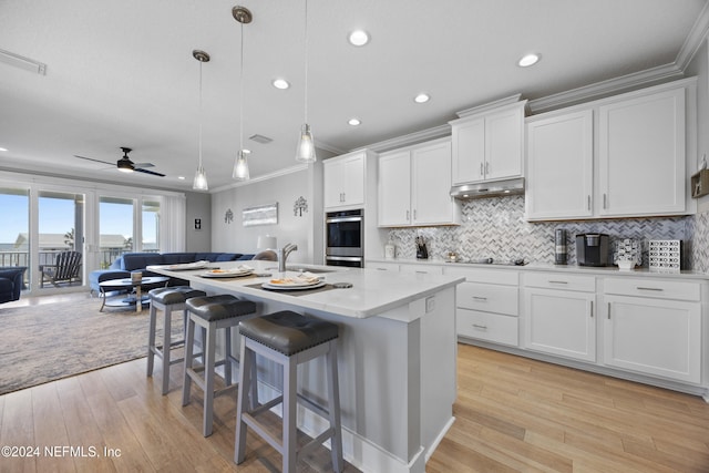 kitchen with a kitchen island with sink, ornamental molding, pendant lighting, white cabinets, and light hardwood / wood-style floors