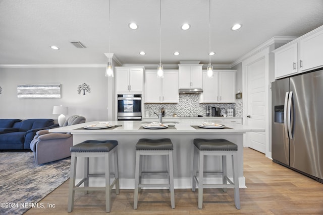 kitchen featuring a center island with sink, white cabinetry, stainless steel appliances, light hardwood / wood-style floors, and decorative light fixtures