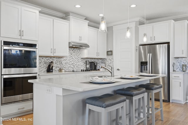 kitchen featuring light hardwood / wood-style flooring, an island with sink, ornamental molding, white cabinetry, and appliances with stainless steel finishes