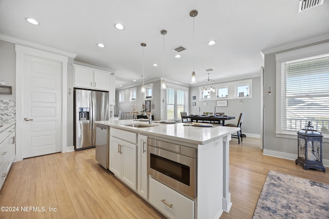 kitchen with appliances with stainless steel finishes, an island with sink, decorative light fixtures, white cabinets, and crown molding