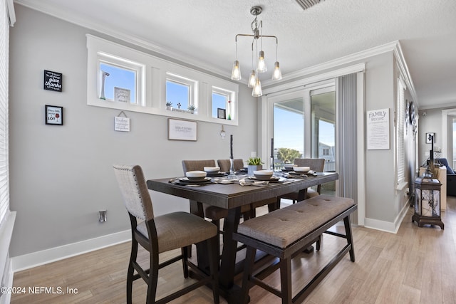 dining space featuring light hardwood / wood-style floors, ornamental molding, a textured ceiling, and a chandelier