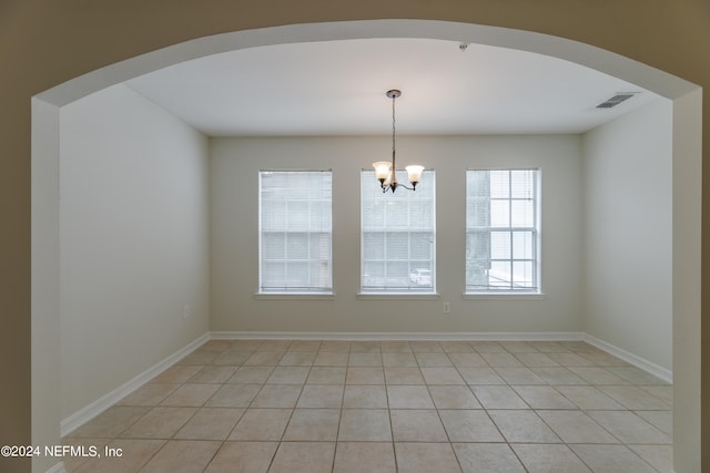 empty room with a notable chandelier and light tile patterned floors