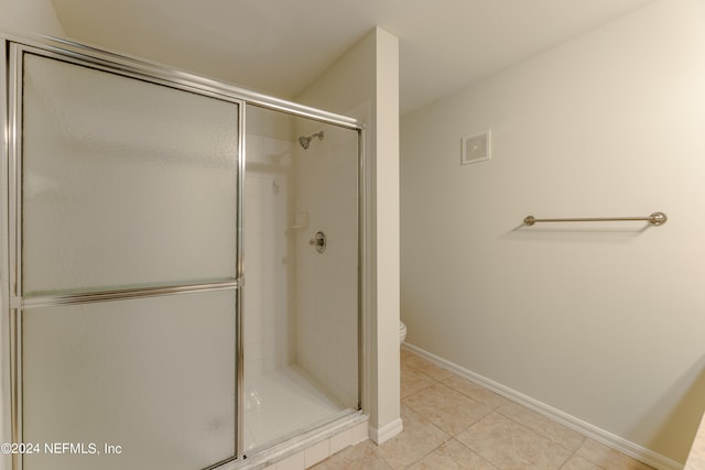 bathroom featuring toilet, a shower with shower door, and tile patterned flooring