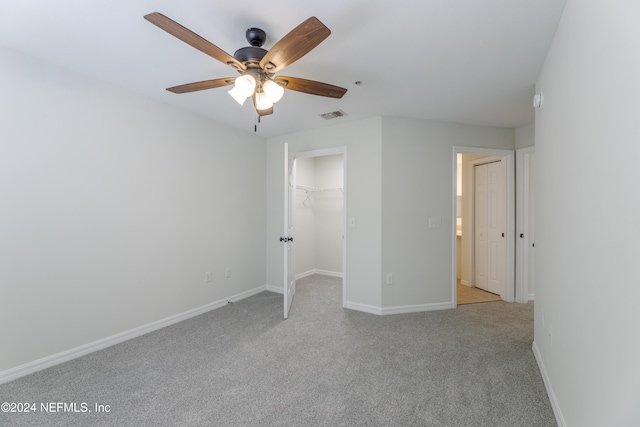 unfurnished bedroom with light carpet, a walk in closet, a closet, and ceiling fan