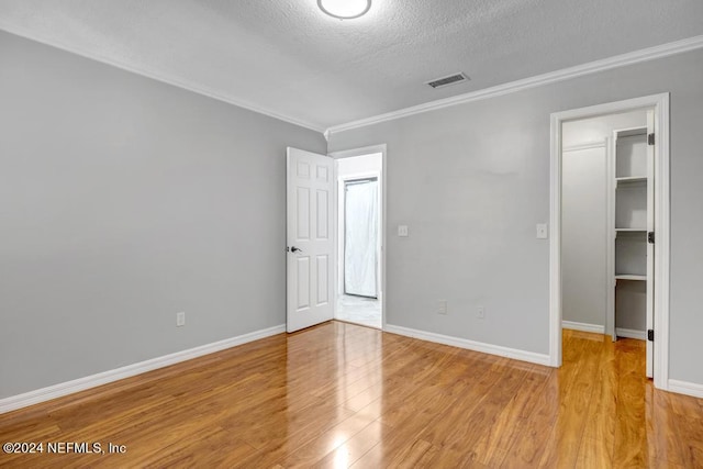 unfurnished bedroom with light wood-type flooring, a spacious closet, a textured ceiling, a closet, and crown molding