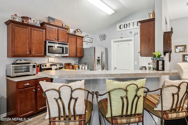 kitchen with stainless steel appliances, vaulted ceiling, a kitchen bar, a textured ceiling, and light hardwood / wood-style floors