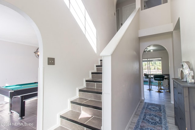 staircase with a high ceiling, wood-type flooring, and billiards