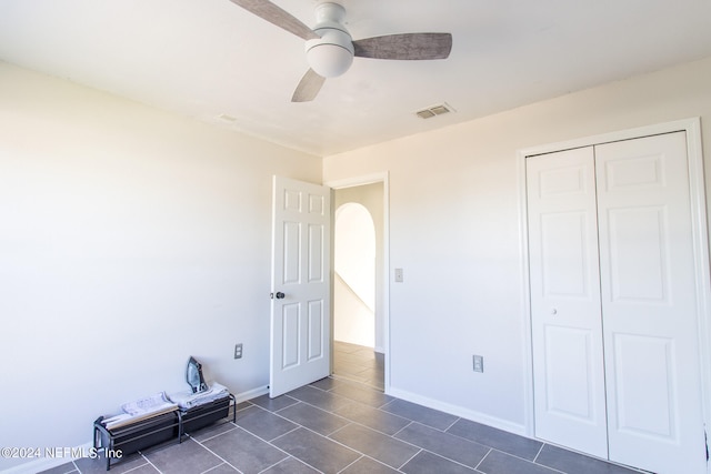 unfurnished bedroom featuring a closet, dark tile patterned floors, and ceiling fan