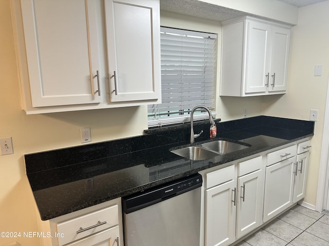 kitchen featuring stainless steel dishwasher, sink, light tile patterned floors, dark stone countertops, and white cabinetry