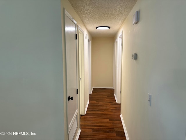 hall with a textured ceiling and dark wood-type flooring