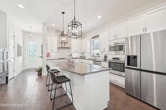 kitchen featuring a kitchen island, hanging light fixtures, stainless steel appliances, white cabinets, and dark wood-type flooring