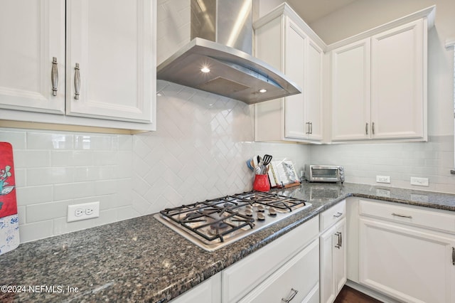 kitchen featuring white cabinets, tasteful backsplash, dark stone counters, stainless steel gas cooktop, and wall chimney exhaust hood