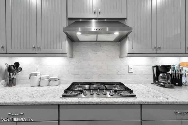 kitchen with wall chimney range hood, tasteful backsplash, gray cabinets, and stainless steel gas cooktop