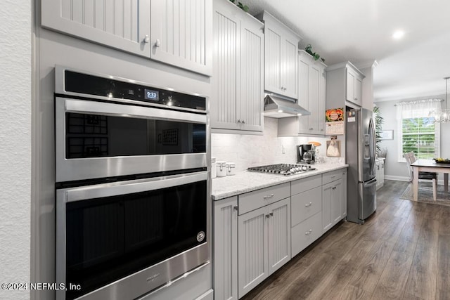 kitchen featuring light stone countertops, appliances with stainless steel finishes, backsplash, dark hardwood / wood-style flooring, and an inviting chandelier