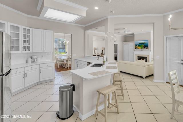 kitchen with ornamental molding, sink, stainless steel fridge, a breakfast bar, and white cabinets