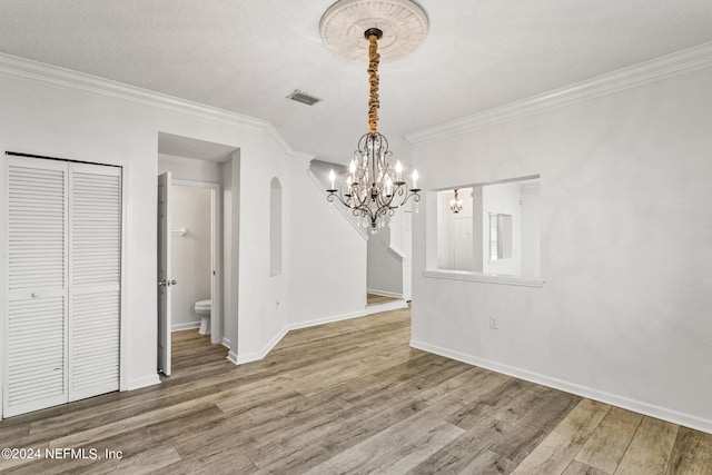 unfurnished dining area with crown molding, a textured ceiling, hardwood / wood-style flooring, and a chandelier