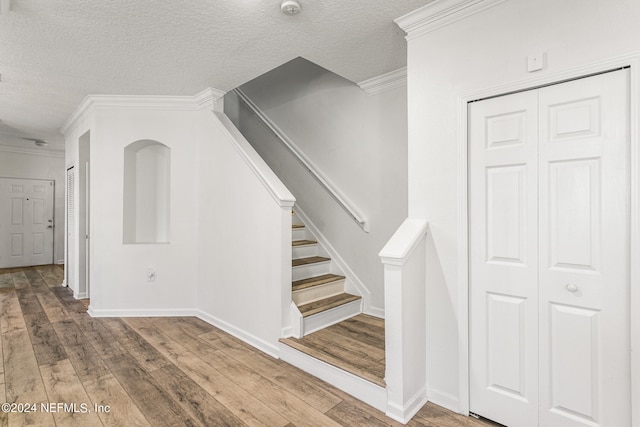 stairway with ornamental molding, hardwood / wood-style floors, and a textured ceiling