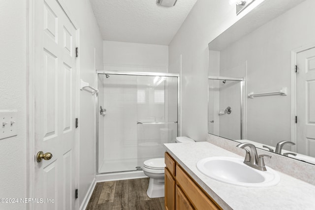 bathroom featuring a shower with door, a textured ceiling, hardwood / wood-style flooring, toilet, and vanity