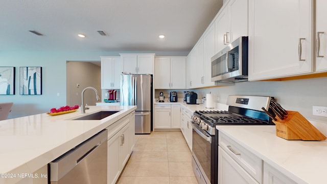 kitchen with appliances with stainless steel finishes, light tile patterned flooring, white cabinetry, and sink