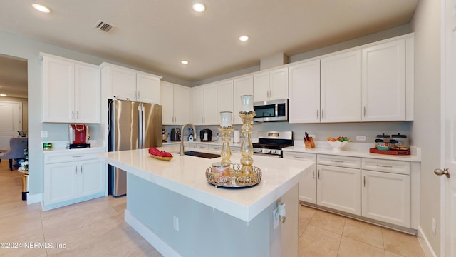 kitchen with white cabinets, a center island with sink, light tile patterned floors, sink, and stainless steel appliances