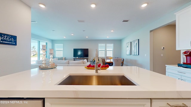 kitchen featuring light stone countertops, sink, a kitchen island with sink, and white cabinets