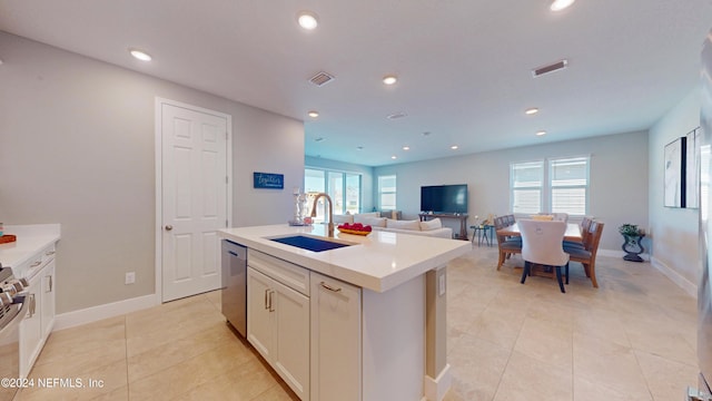 kitchen with sink, white cabinetry, stainless steel dishwasher, light tile patterned floors, and a center island with sink