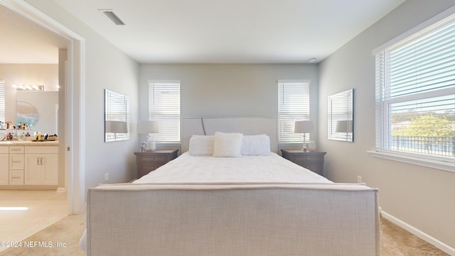 bedroom featuring light carpet, multiple windows, and ensuite bath