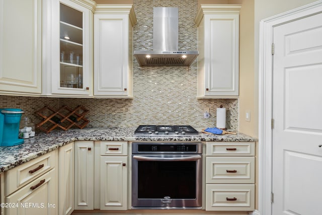 kitchen featuring light stone counters, stainless steel appliances, wall chimney range hood, and tasteful backsplash