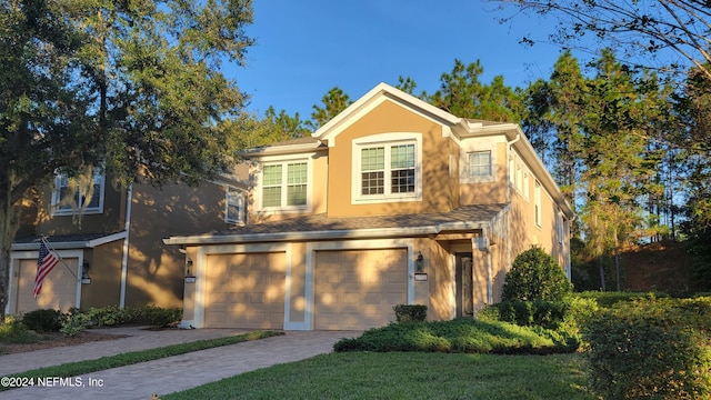 traditional home with decorative driveway, a garage, and stucco siding