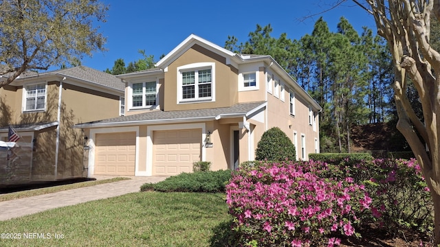 traditional home featuring a shingled roof, decorative driveway, a garage, and stucco siding